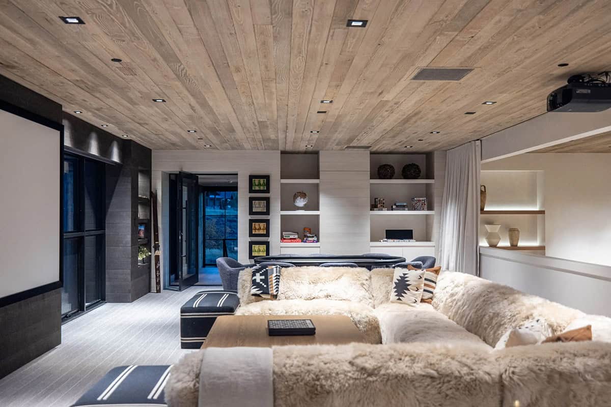 Lower-level media room with shearling sectional sofa, wood plank ceiling, projection screen, and game table