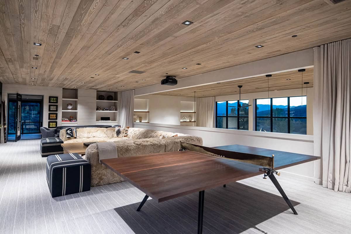 Rec room with ping pong table, shearling sofa, wood ceiling, and mountain views through clerestory windows