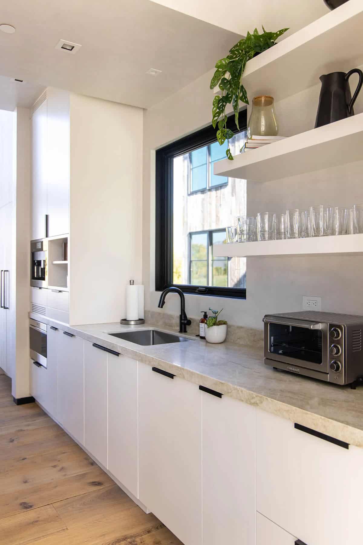 Scullery kitchen with white cabinetry, stone countertops, black faucet, and open shelving with glassware