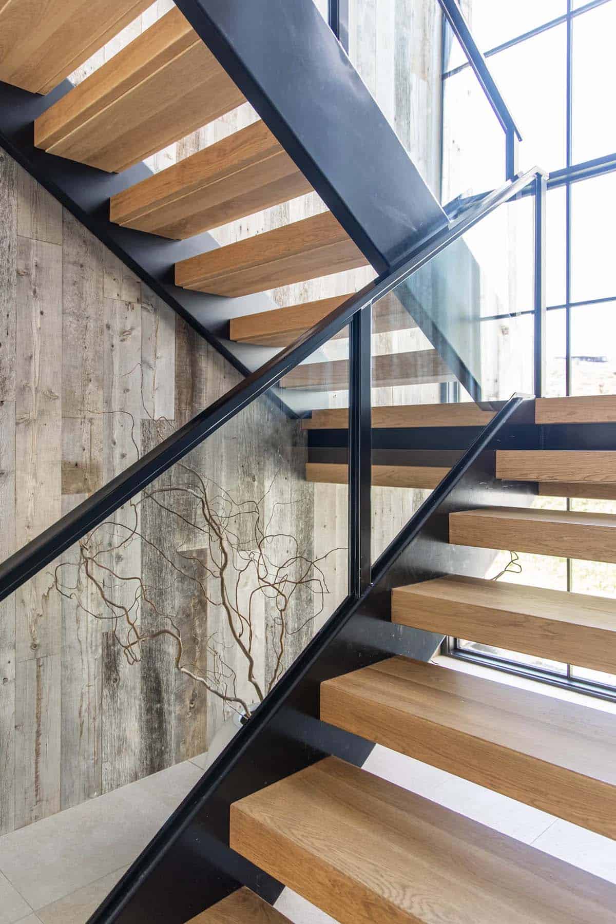 Floating oak staircase with black steel stringers, glass railing, and reclaimed wood accent wall