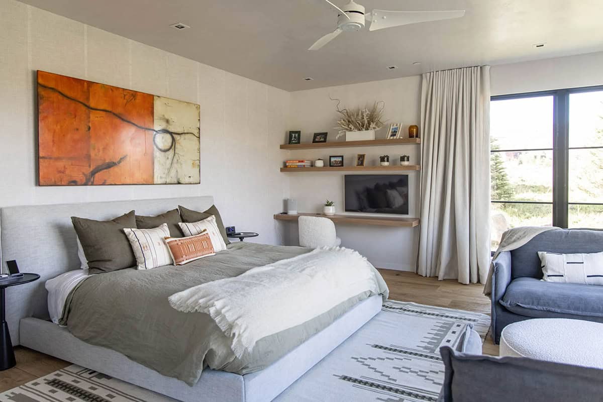Primary bedroom with upholstered platform bed, large abstract artwork, floating oak shelves, and sliding glass door