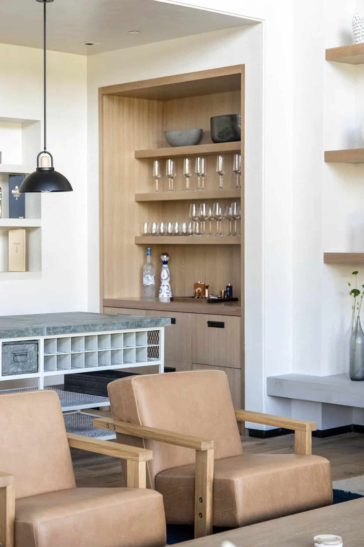 Built-in white oak bar niche with stemware shelves and galvanized metal bar cart with stone top