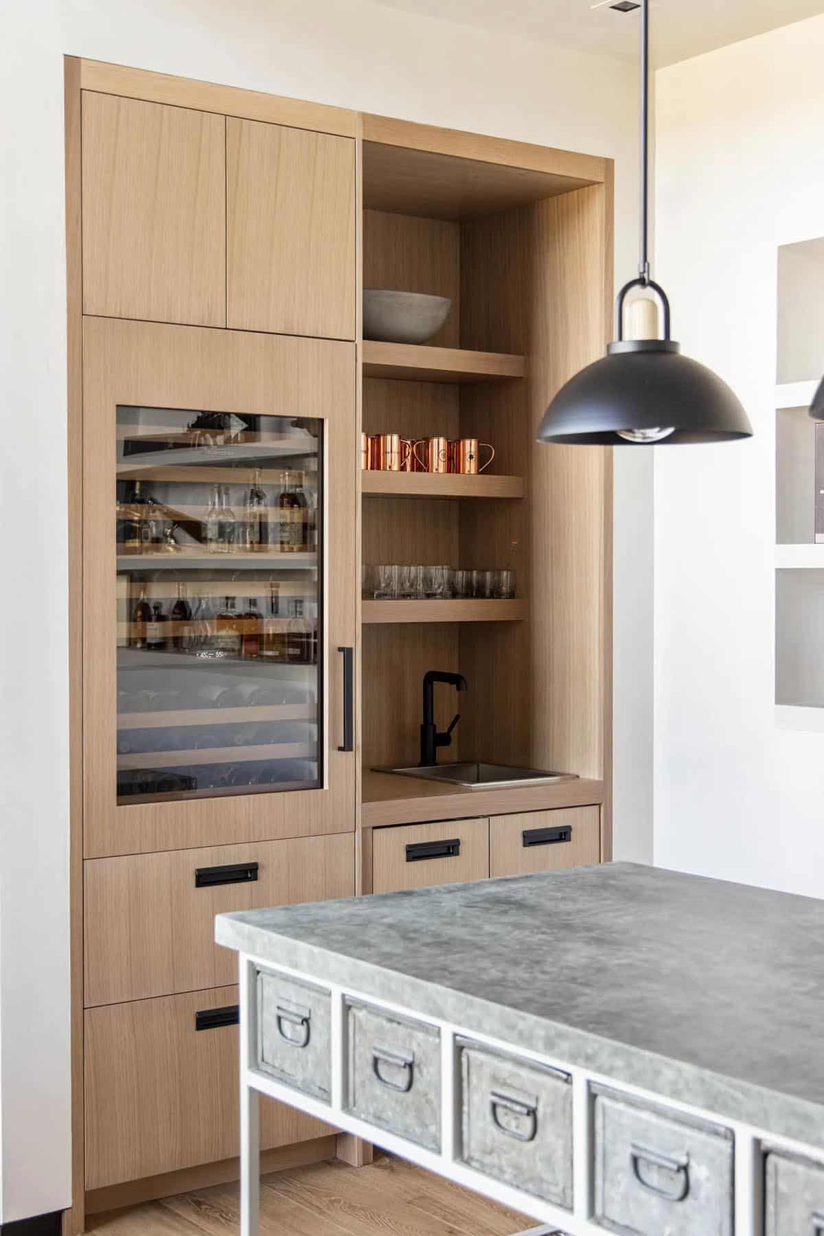 White oak wet bar with glass-front wine fridge, open shelving, copper mugs, and black faucet at small sink