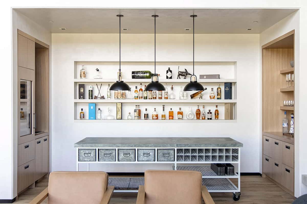 Bar room with recessed spirit shelf, galvanized metal rolling bar cart, black dome pendants, and flanking oak cabinetry
