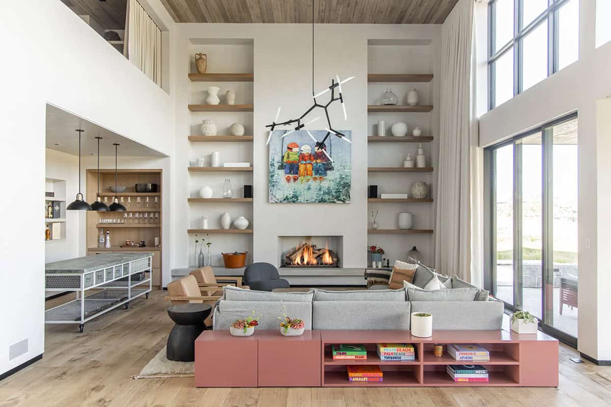Double-height great room with gray sectional, terracotta media console, floor-to-ceiling bookshelves, and lit fireplace