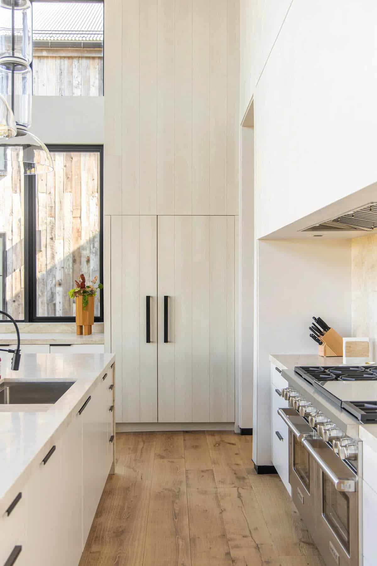 Kitchen galley with floor-to-ceiling white paneled pantry cabinet, pro range, stone backsplash, and black hardware