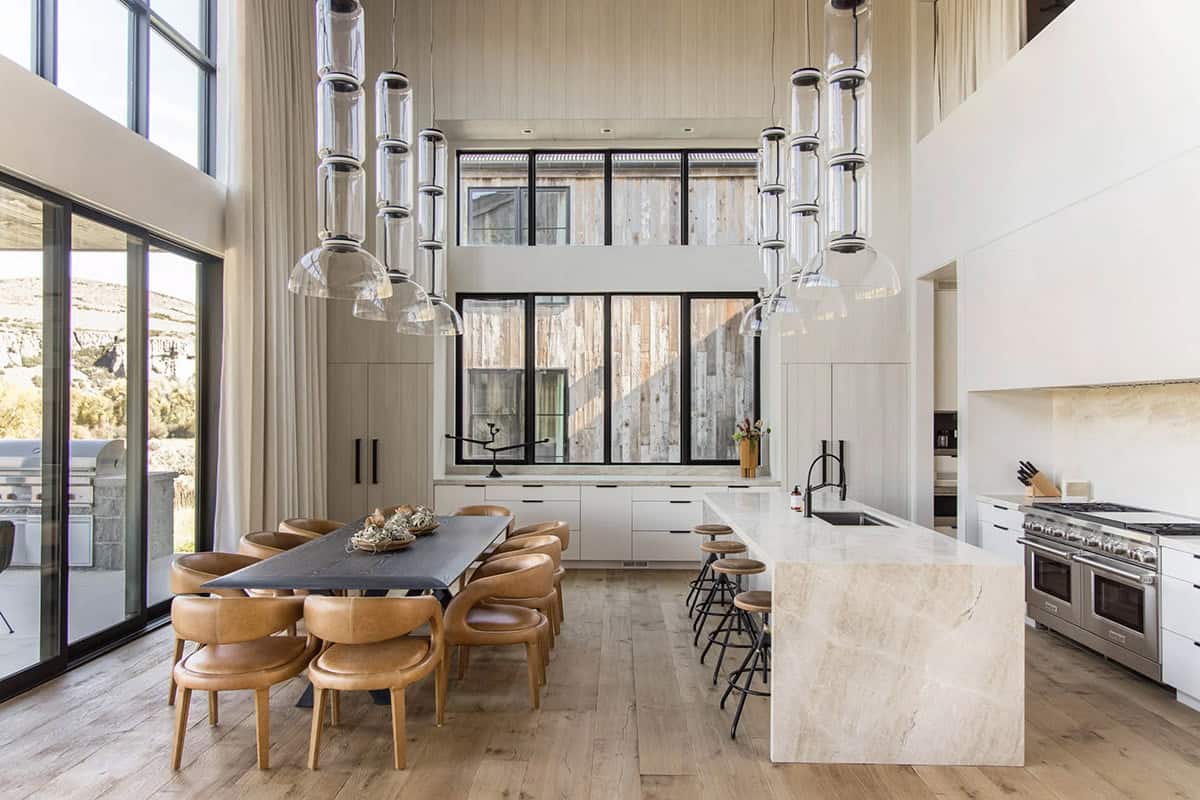 Full kitchen and dining overview with travertine island, leather dining chairs, stacked glass pendants, and reclaimed wood accent wall