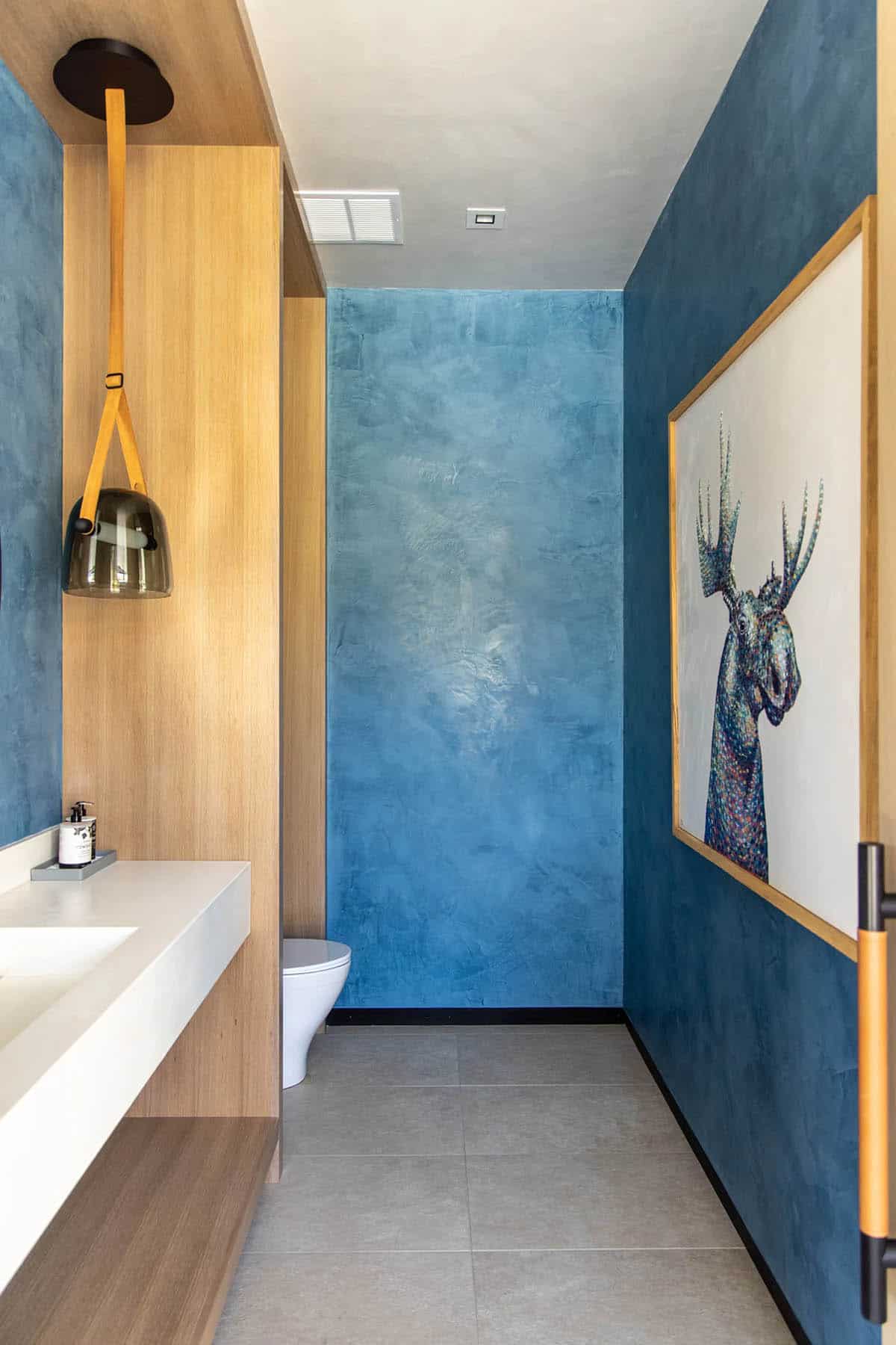 Blue plaster powder room with smoked glass pendant, floating vanity, wall-mounted toilet, and colorful moose portrait
