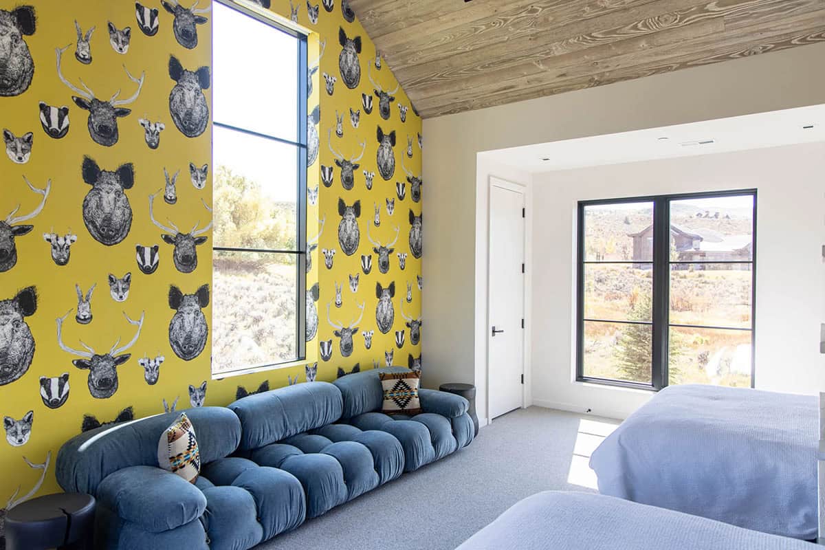 Kids bedroom with bold yellow wildlife wallpaper, blue tufted low sofa, wood plank ceiling, and mountain views