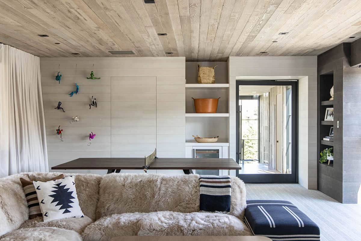 Lower-level game room with shearling sectional, ping pong table, colorful climbing figure wall art, and built-in shelving