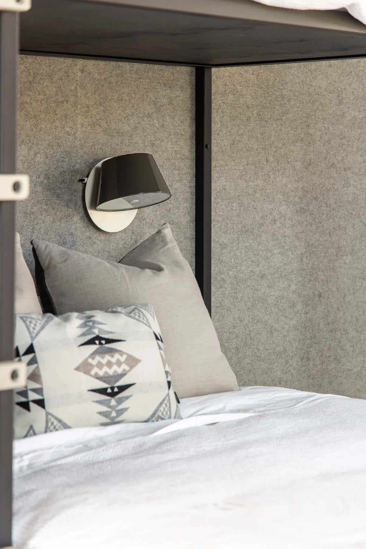 Close-up of bunk bed niche with felt upholstered back panel, adjustable reading sconce, and Navajo-print pillow