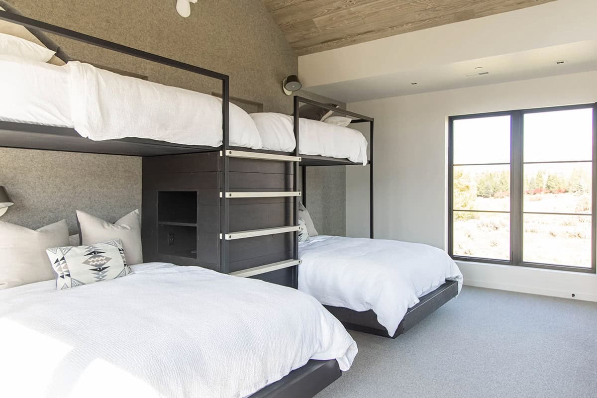 Custom black steel bunk beds with felt-lined alcoves, integrated ladder, built-in shelf, and mountain views through window
