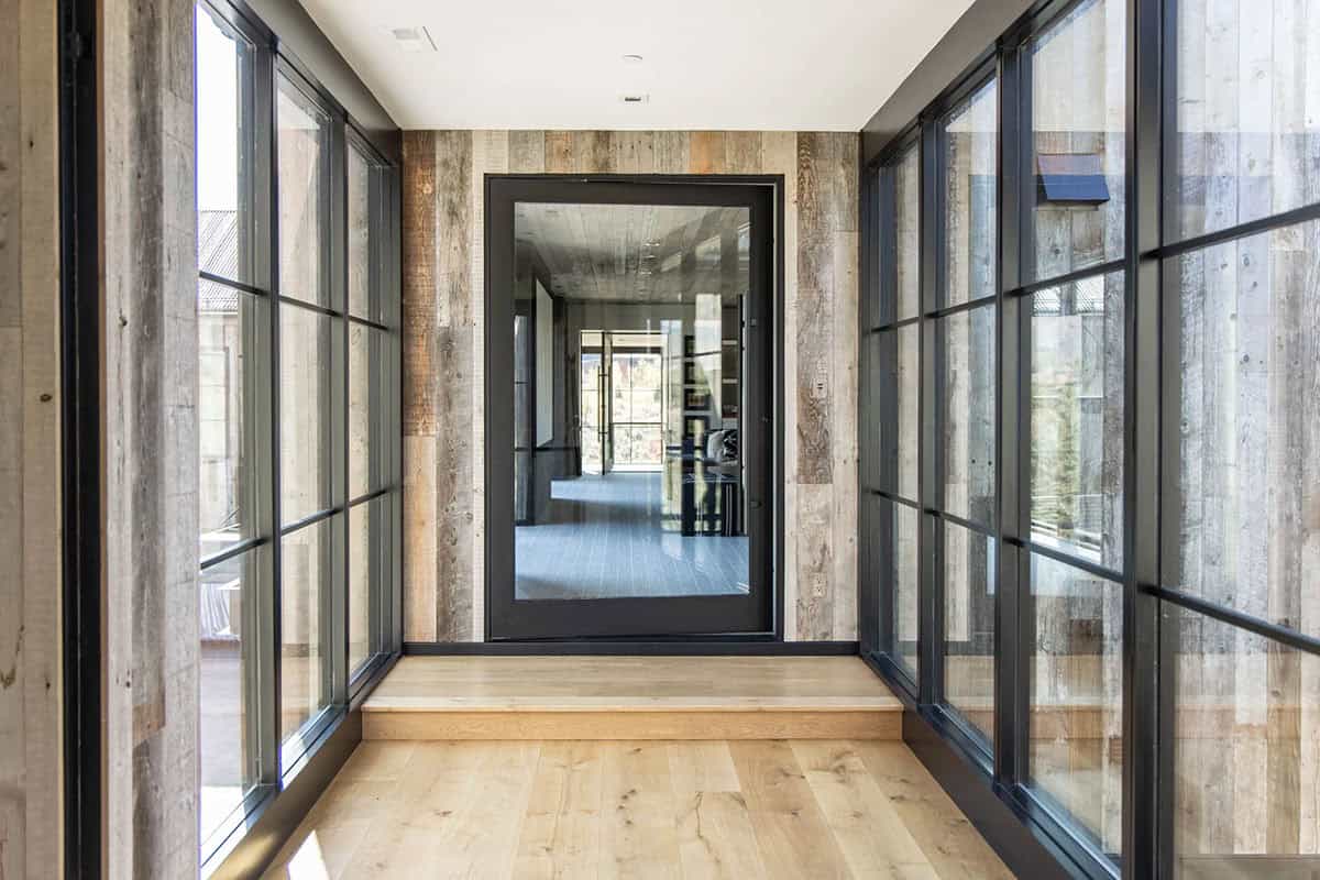 Glass-lined entry corridor with reclaimed wood accent wall, black steel door, and oak hardwood floors