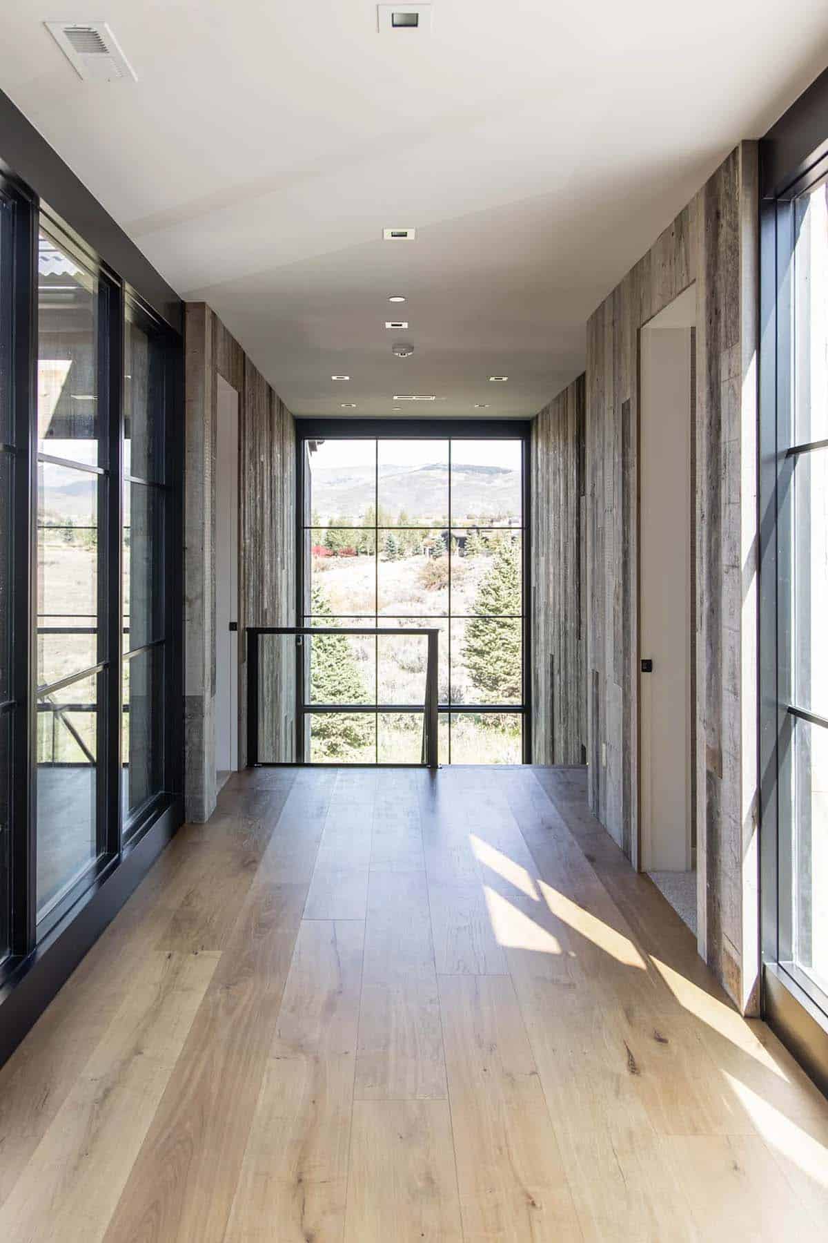 Upper hallway lined with reclaimed wood paneling, steel-framed windows, and mountain views at the end
