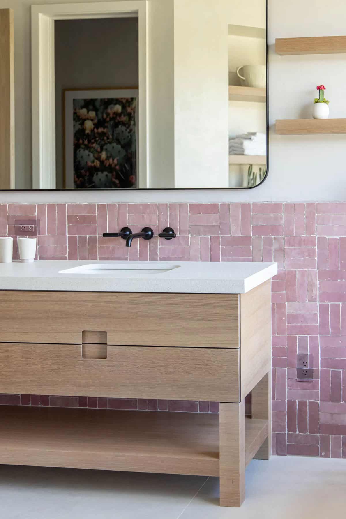 White oak bathroom vanity with quartz countertop, wall-mounted black faucet, and pink zellige tile backsplash