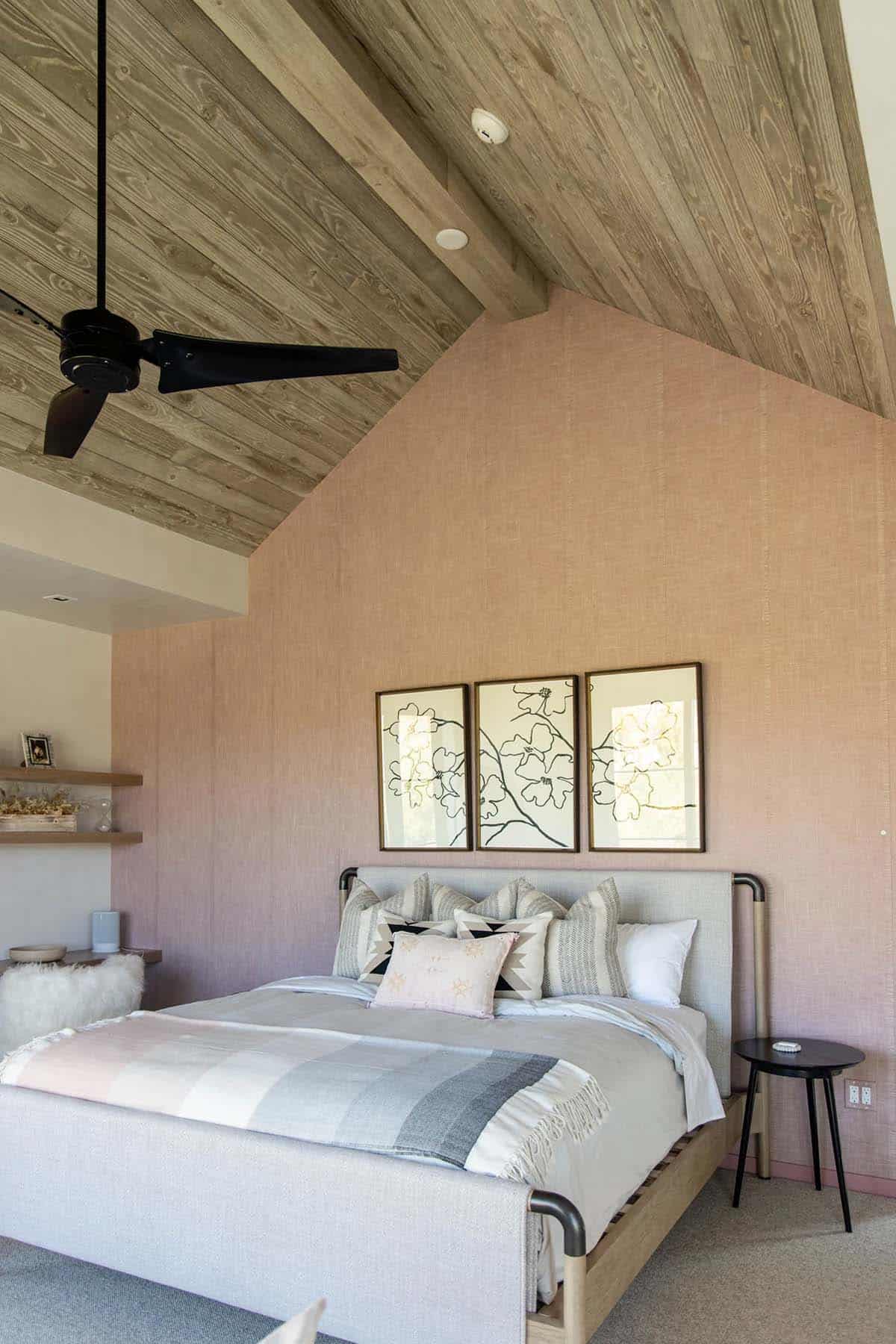 Girl's bedroom with blush grasscloth accent wall, vaulted wood ceiling, upholstered bed frame, and triptych floral artwork