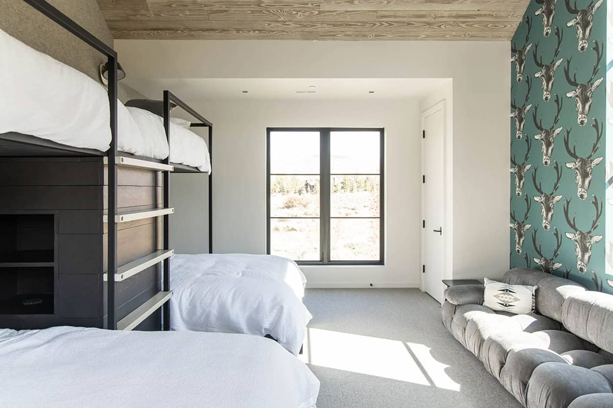 Bunk room with black steel bunk beds, teal stag-print wallpaper accent wall, and low gray tufted sofa