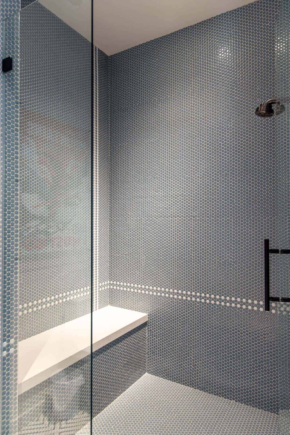 Walk-in shower with floor-to-ceiling slate blue penny tile, white built-in bench, and chrome showerhead