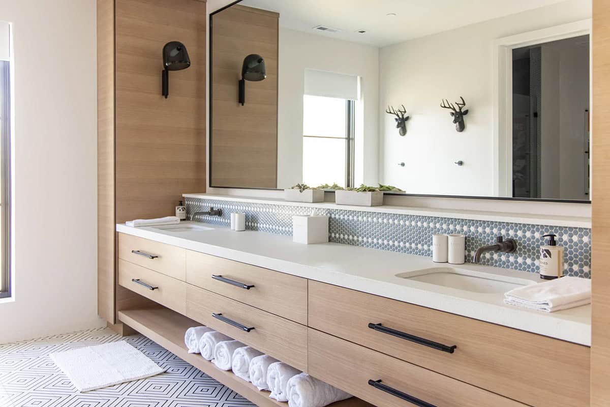 Kids bathroom double vanity with white oak cabinetry, penny tile backsplash, geometric floor tile, and black deer head wall hooks