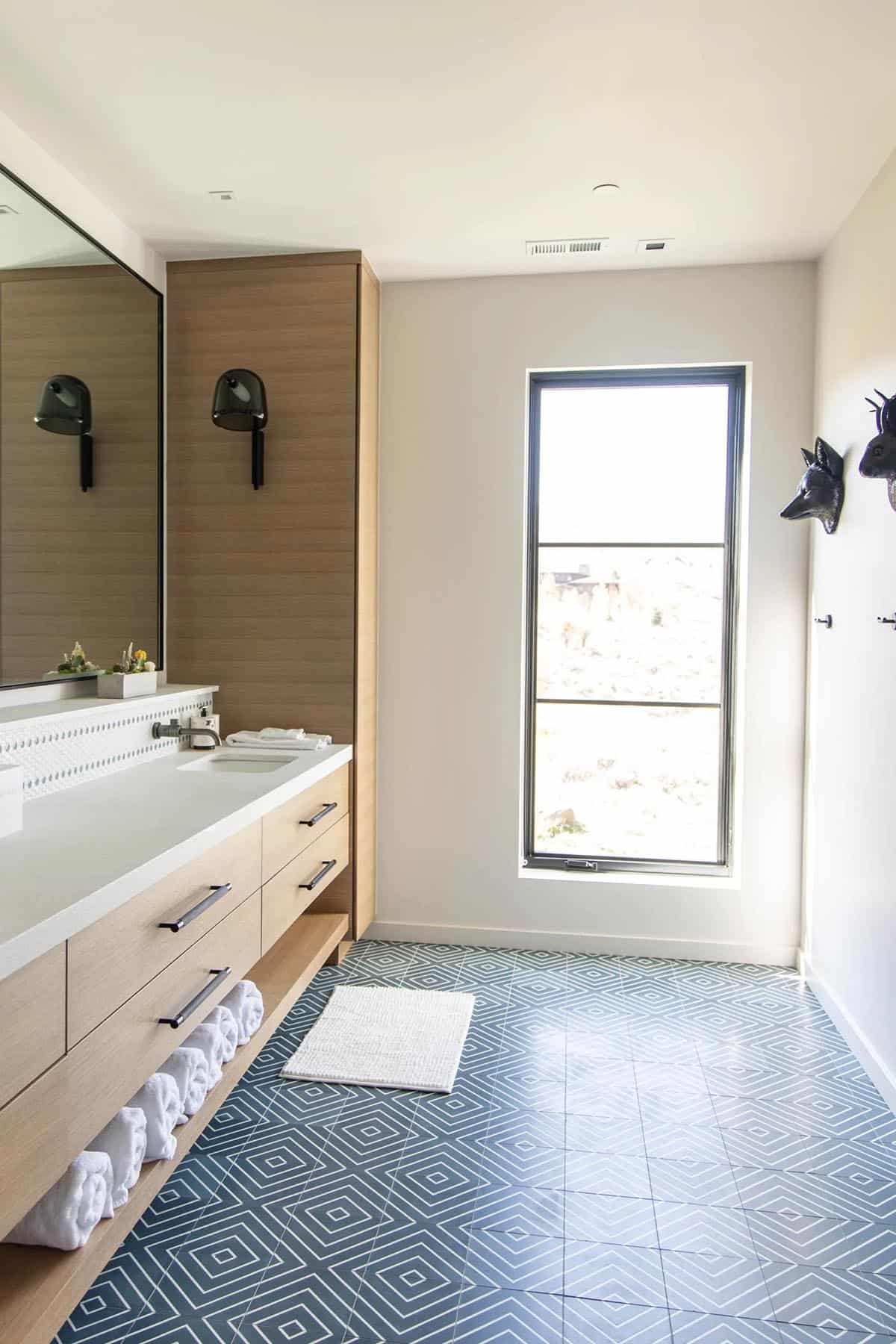 Kids bathroom with white oak vanity, blue diamond-pattern floor tile, tall window, and black fox wall hook