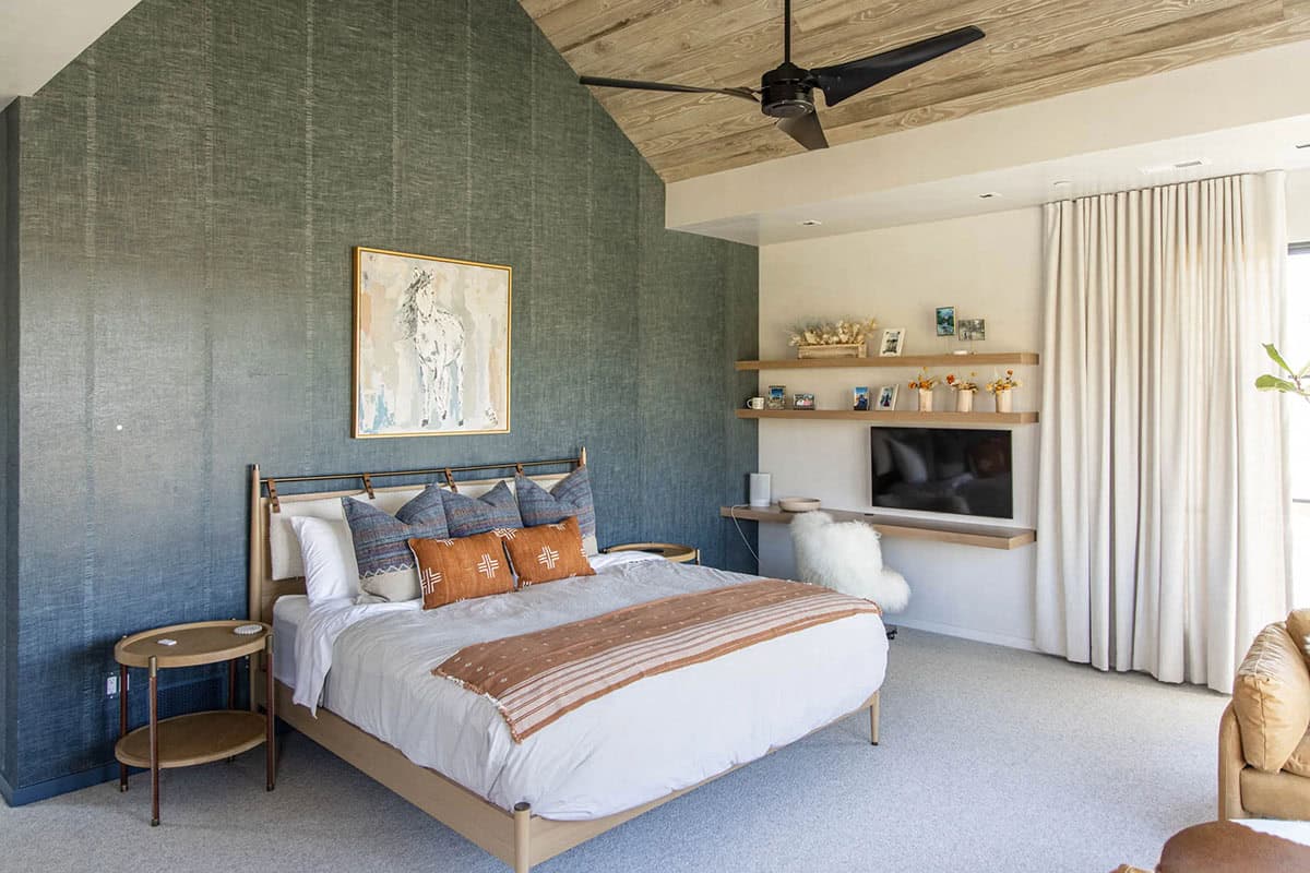 Guest bedroom with teal grasscloth vaulted accent wall, wood-framed bed, rust mud cloth pillows, and horse painting