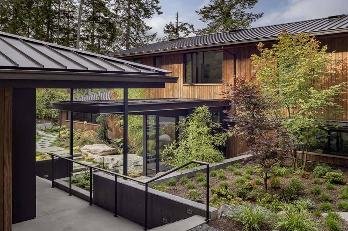 Covered breezeway with steel-framed glass connector linking house wings over a Japanese-inspired courtyard garden