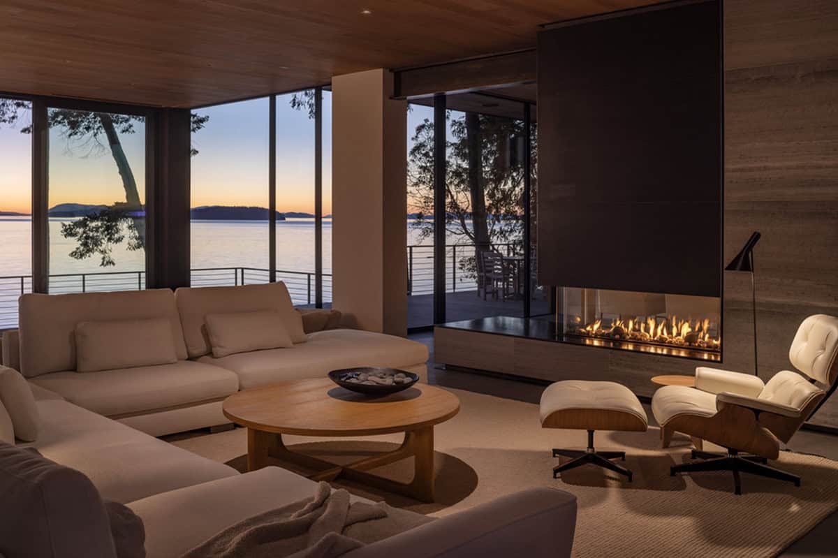 Living room at dusk with linear gas fireplace, Eames lounge chair, and glowing sunset over the water