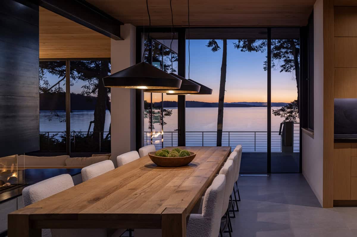 Dining room at sunset with large pendant light over oak table, floor-to-ceiling water-view windows