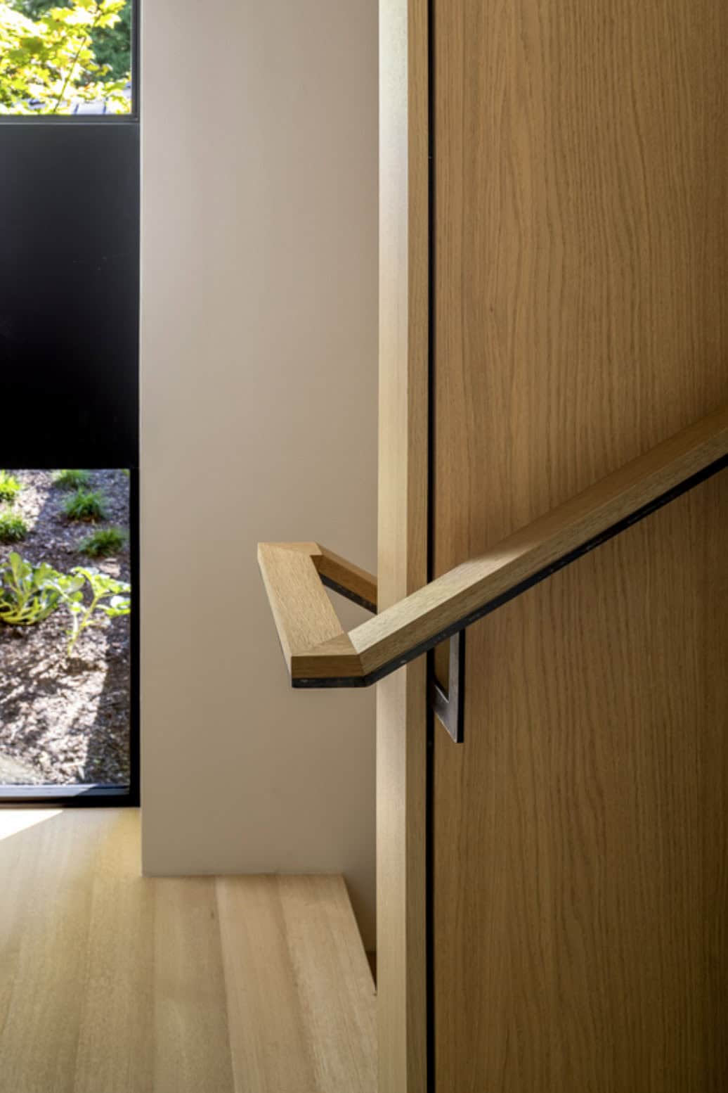 Detail of custom angular oak door pull with black metal bracket against white wall
