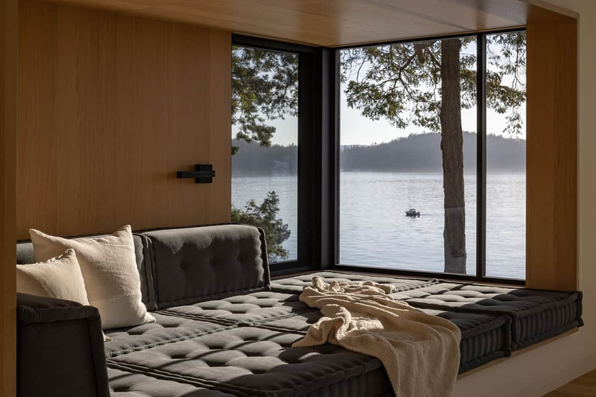 Built-in daybed nook with tufted dark cushions and corner windows overlooking calm water and islands 