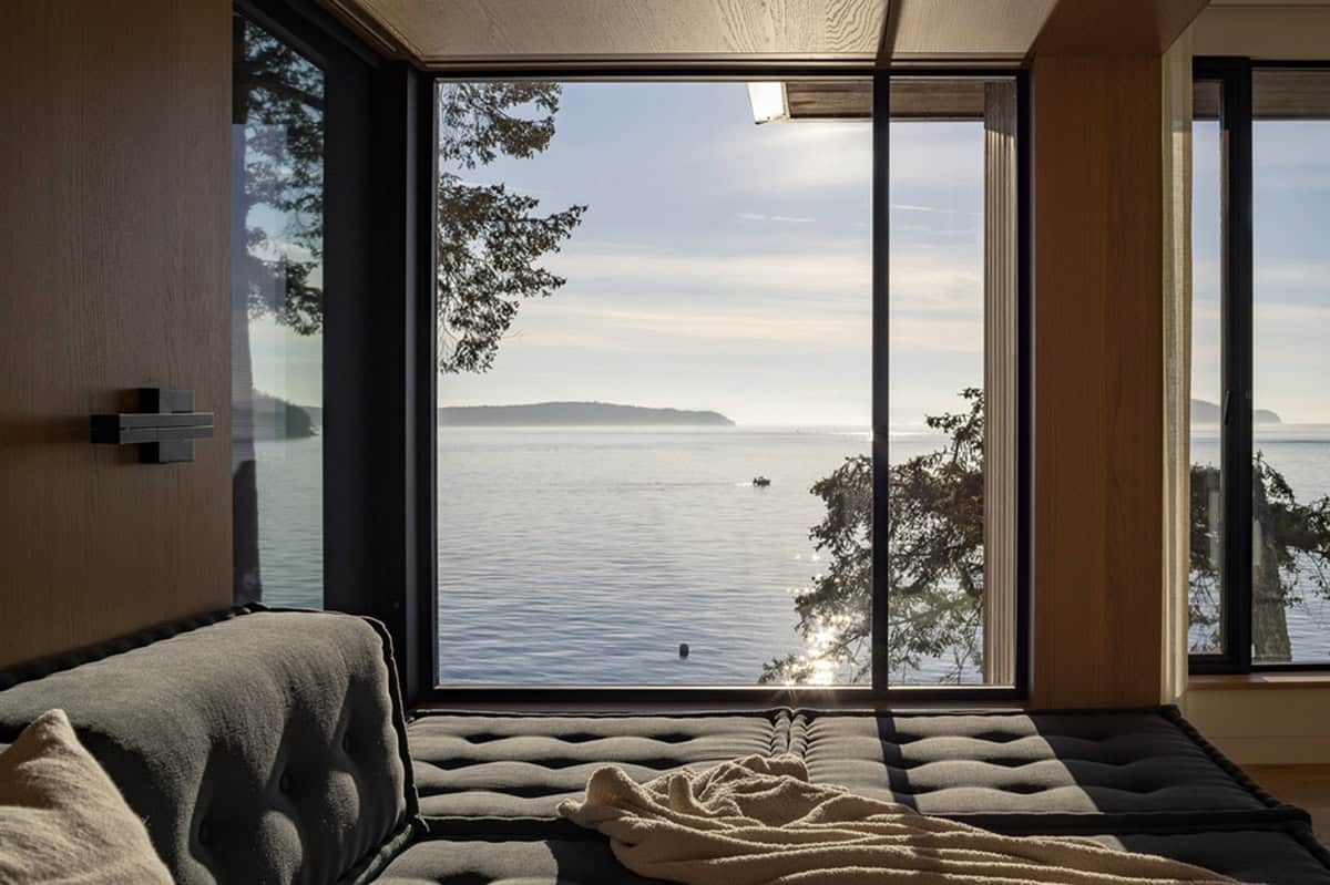 View from tufted daybed through large picture window to serene bay with distant island silhouettes