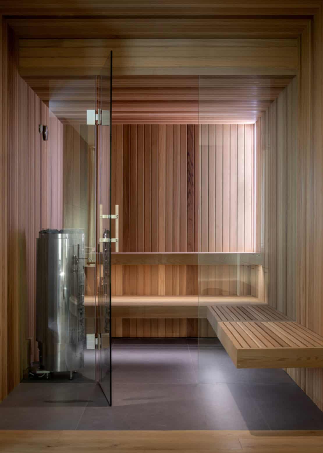 Cedar-lined private sauna with glass door, tiered wood benches, and stainless steel heater