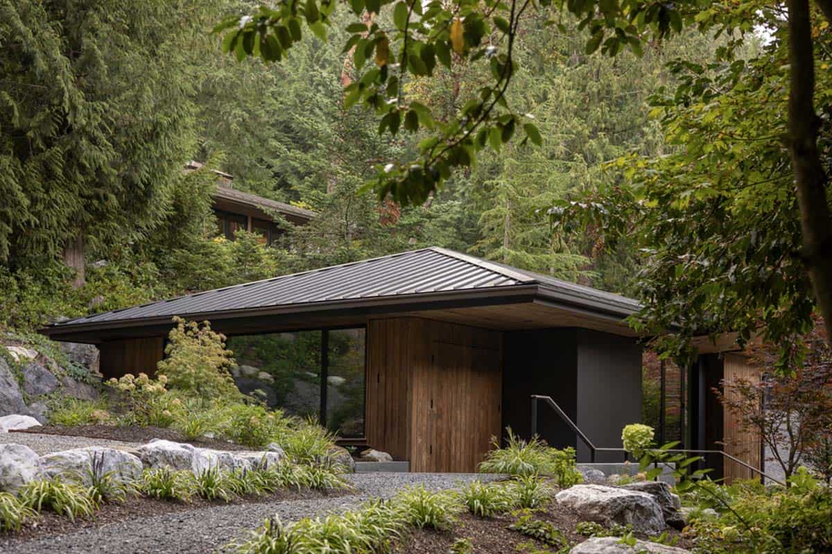 Low-profile guest cottage with dark metal hip roof nestled among boulders and native garden plantings