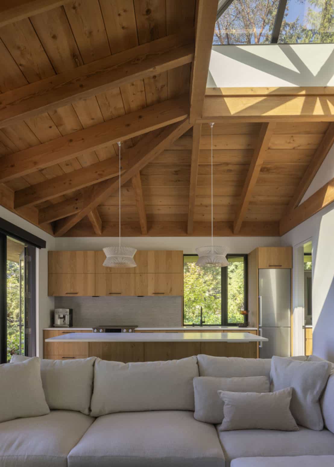 Guest cottage interior with exposed wood beam cathedral ceiling, open kitchen, and cream sectional sofa