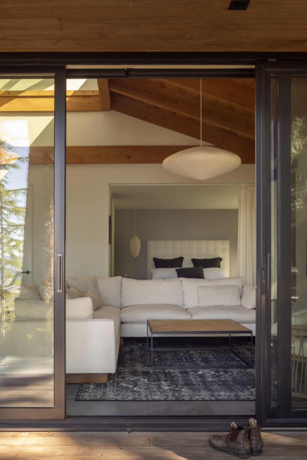 View through open sliding glass door into guest cottage living room with vaulted beam ceiling and pendant light