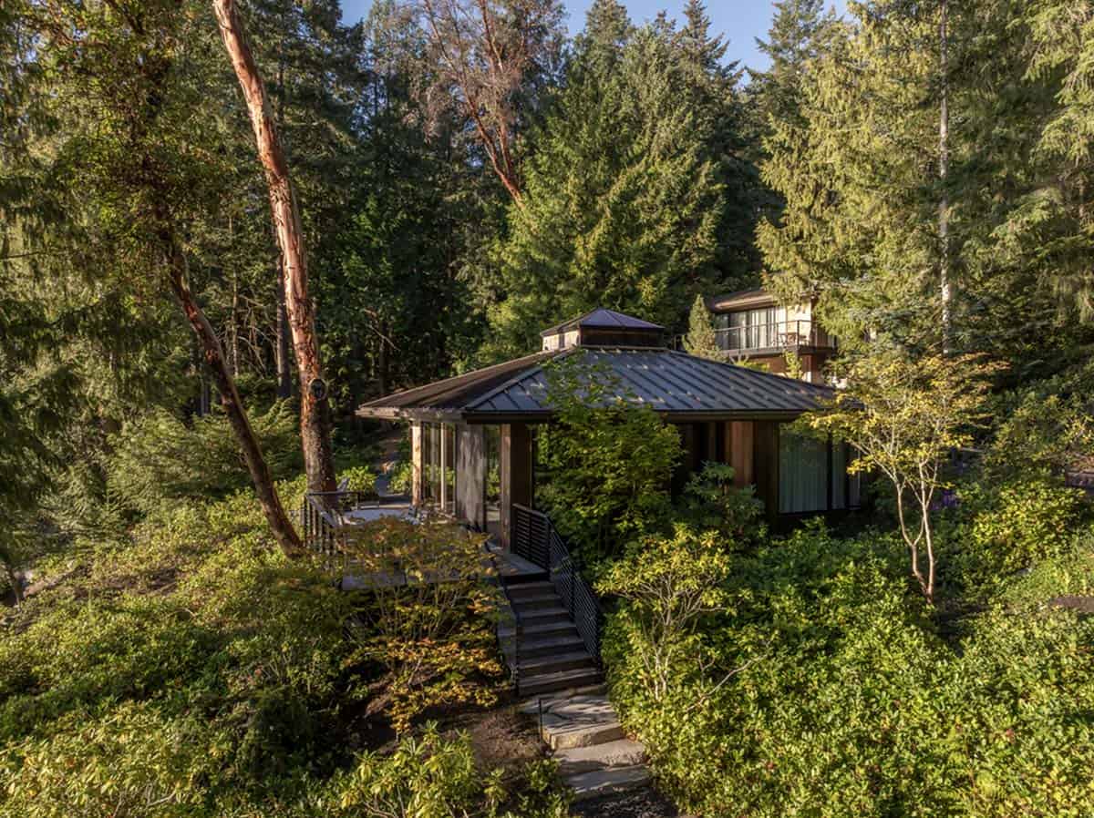 Aerial view of guest cottage with dark hip roof surrounded by lush Pacific Northwest forest and stepping stone path