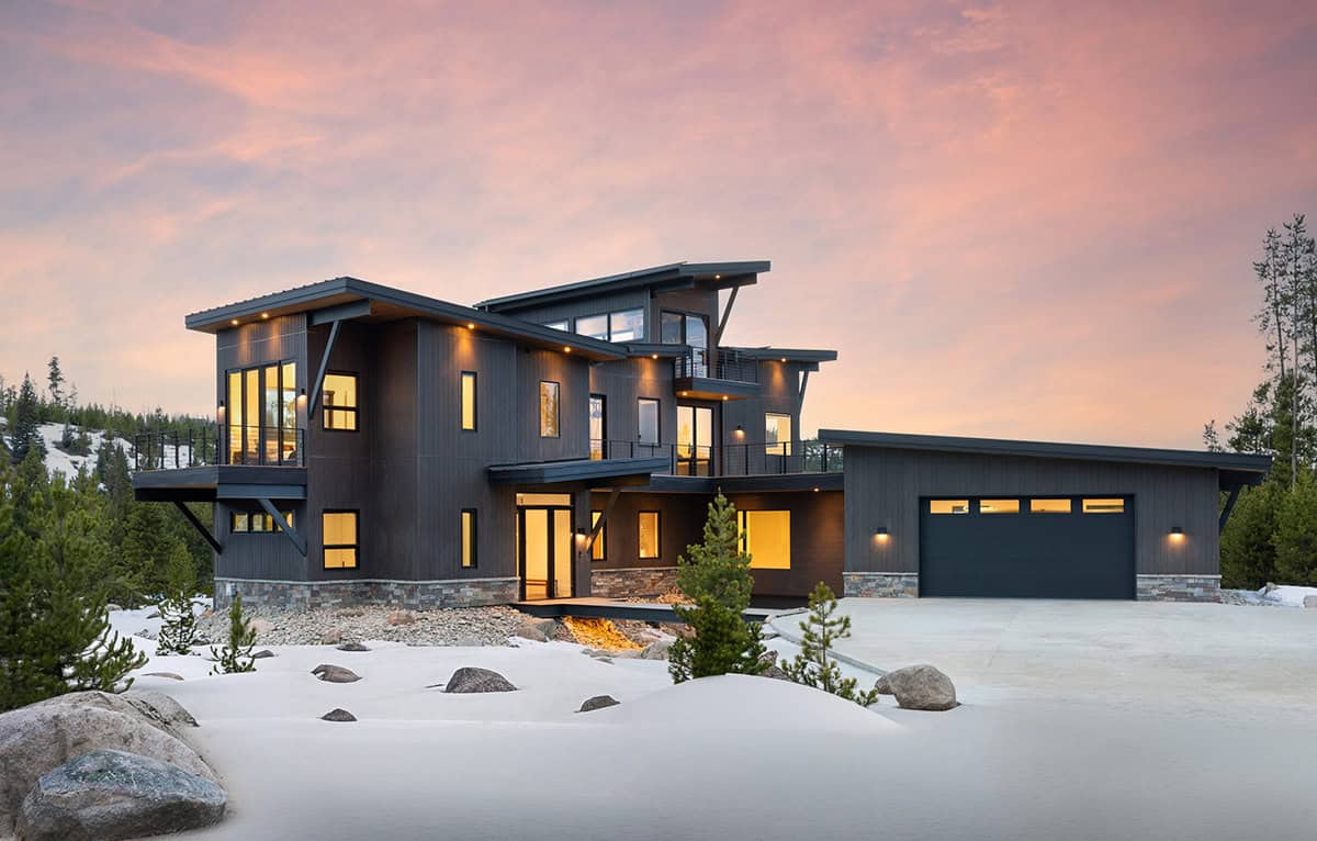 Cloudwalk mountain contemporary home exterior at dusk with snow, dark siding and glowing windows, designed by MA Studios in Granby, Colorado