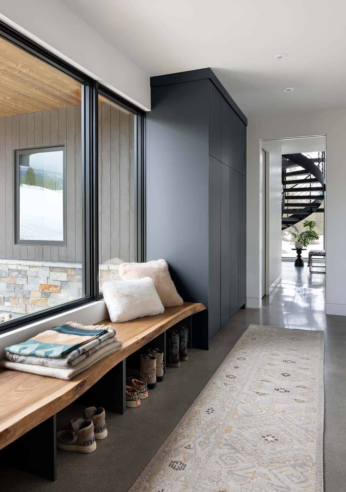 Mudroom entryway with live-edge wood bench, dark built-in cabinetry, and snowy mountain view through black-framed window