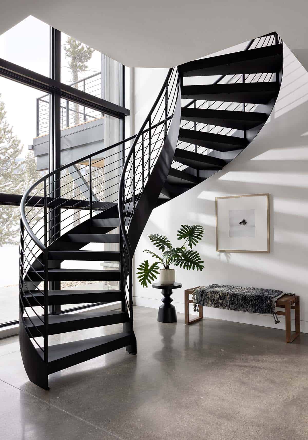 Dramatic black steel spiral staircase with floor-to-ceiling windows and polished concrete floors in Cloudwalk home