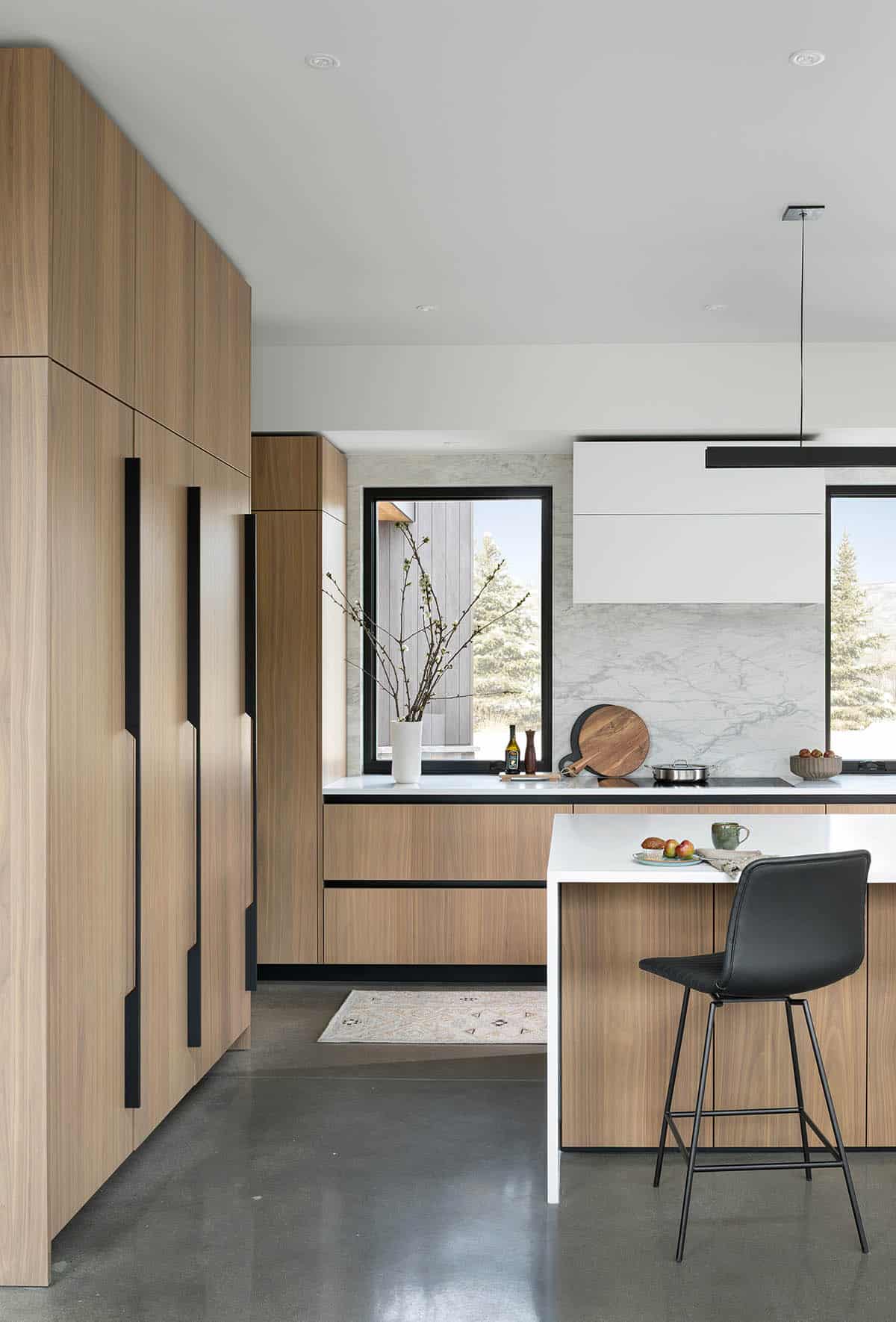 Close-up of flat-front wood kitchen cabinetry with black hardware, marble backsplash, and white island