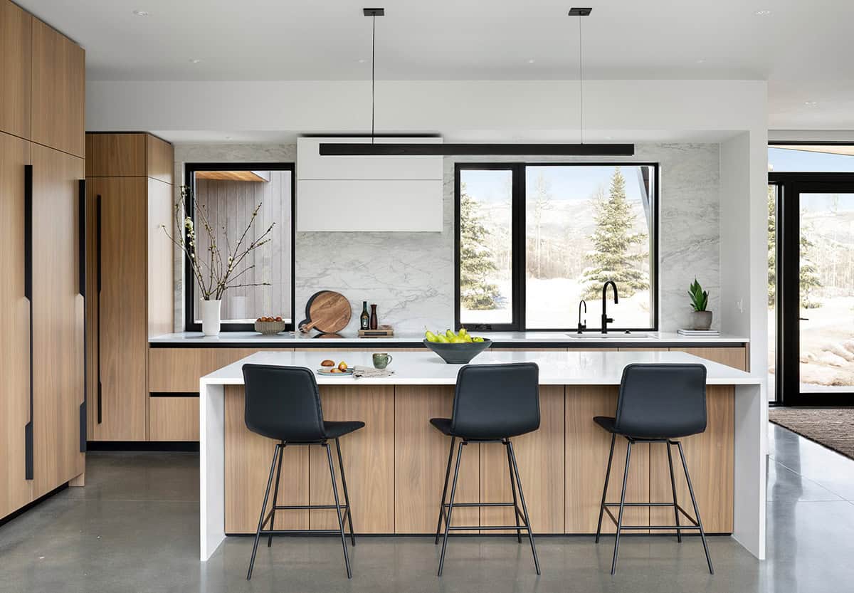 Kitchen island with black bar stools, wood cabinetry, marble backsplash, and snowy mountain views through windows