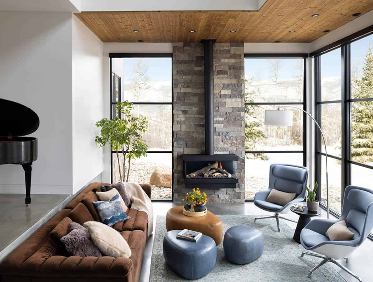 Sunken living room with stacked stone fireplace, brown velvet sofa, blue lounge chairs, and floor-to-ceiling windows