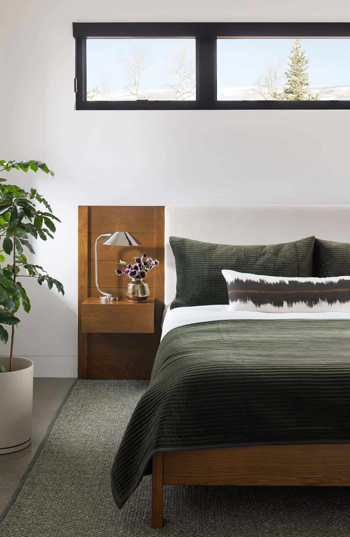 Primary bedroom detail with upholstered headboard, green velvet bedding, floating wood nightstand, and clerestory window