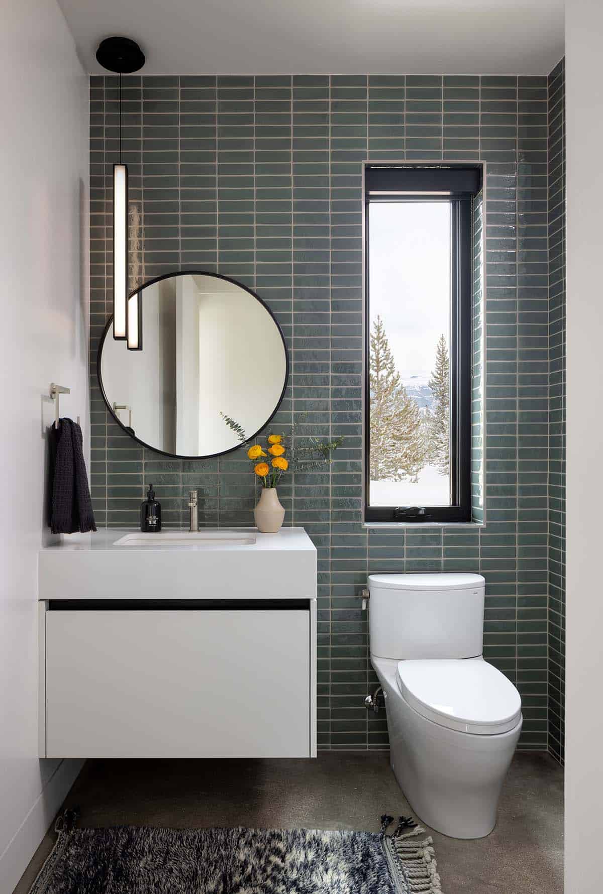 Modern powder room with sage green stacked tile, round mirror, floating white vanity, and narrow black-framed window
