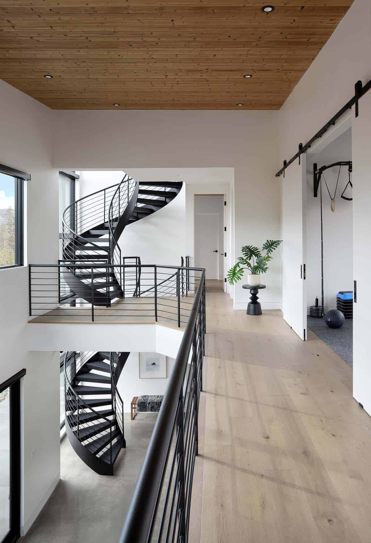Second-floor landing with black steel spiral staircase, wood ceiling, and barn door leading to home gym