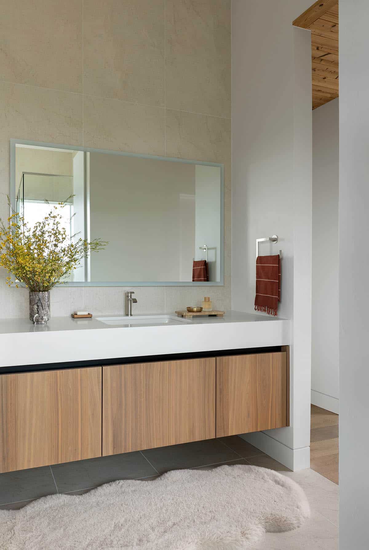 Primary bathroom floating wood vanity with white countertop, large format tile walls, and wood plank ceiling detail