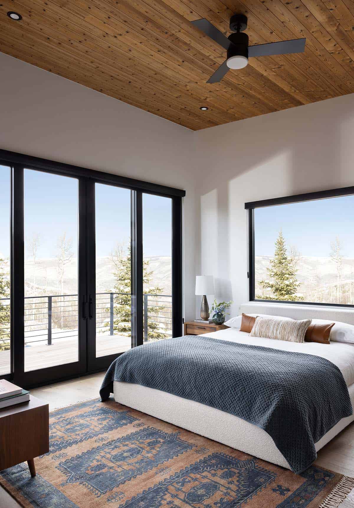 Primary bedroom with wood plank ceiling, floor-to-ceiling sliding glass doors opening to balcony with mountain views