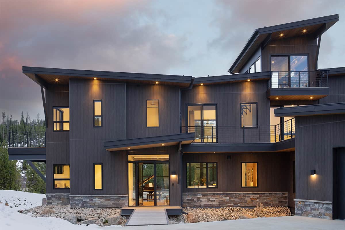 Rear exterior of Cloudwalk home at dusk showing staggered rooflines, illuminated windows, and snowy Colorado landscape