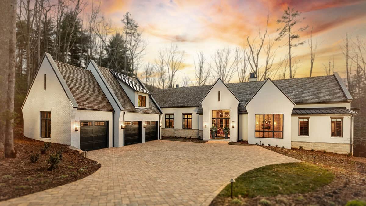 Mountain modern home exterior at dusk with white brick, dark garage doors, and stone driveway