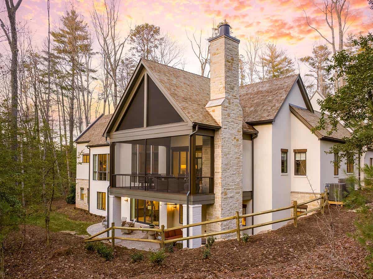 Rear view of mountain modern home with screened porch, stone chimney, and wooded backdrop